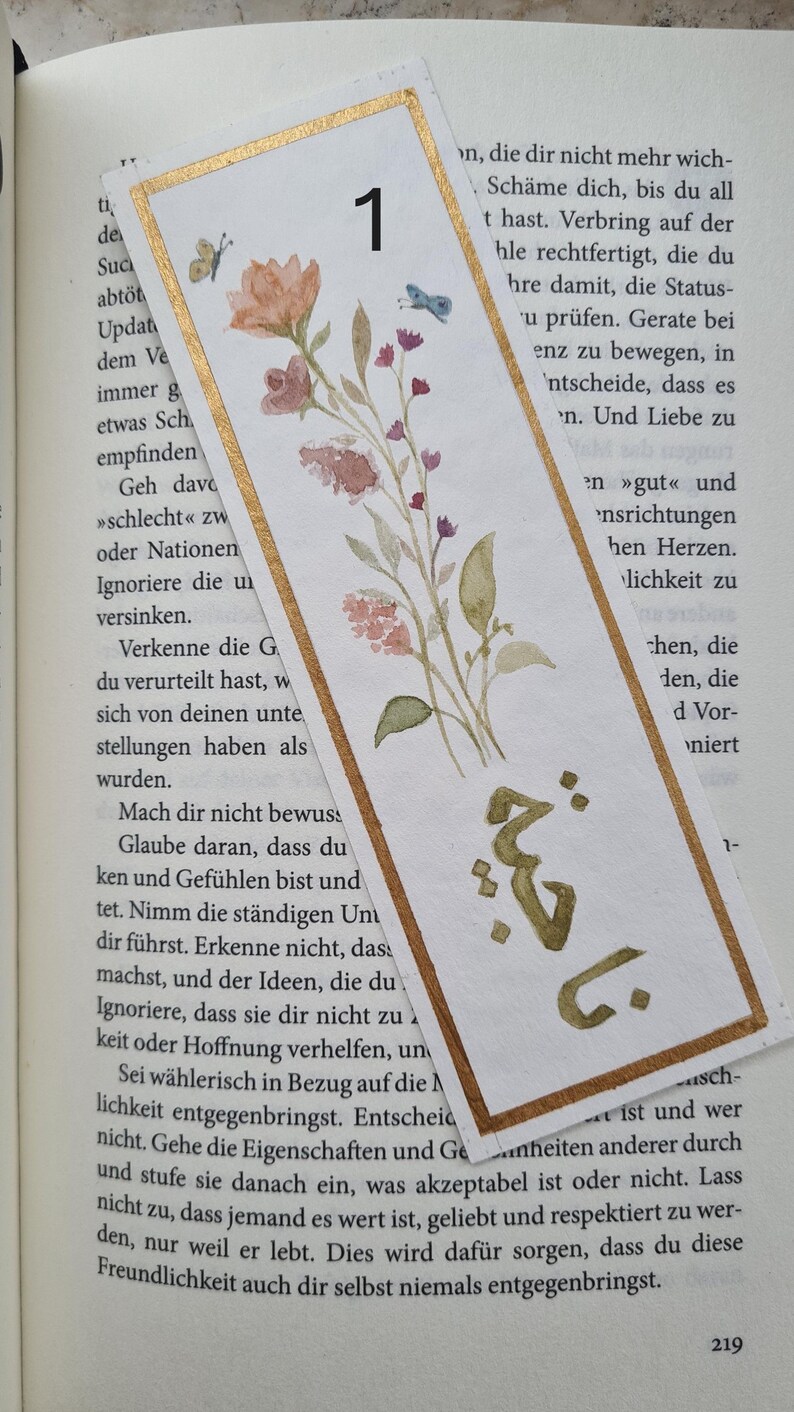 May include: A watercolour illustration of a floral bouquet with a gold border and the number "1" in the top right corner. The text "Mach dir nicht bewusst" is visible in the lower left corner.