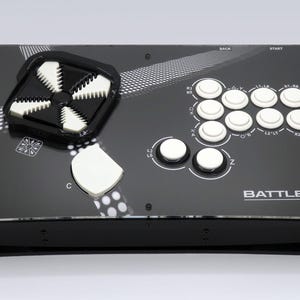 Puede incluir: Controlador de arcade negro con botones blancos y un diseño único en blanco y negro. El controlador tiene el texto "BATTLEHUT BHT". Cuenta con un joystick y varios botones para jugar.