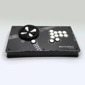 Può includere: Un controller di gioco rettangolare nero dotato di un pad direzionale circolare con un inserto bianco a forma di croce, molteplici pulsanti di azione circolari bianchi e il testo BATTLEHUT BH-T22 stampato in bianco sulla parte superiore.