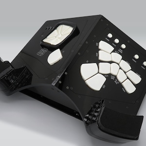 Puede incluir: Máquina de ritmo electrónica negra con almohadillas y botones blancos. La máquina de ritmo tiene dos altavoces a los lados.