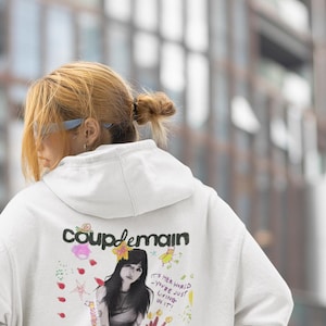 May include: White hoodie with a colourful graphic print featuring a cartoon character and the text "coup de main" and "BEABADOOBEE".