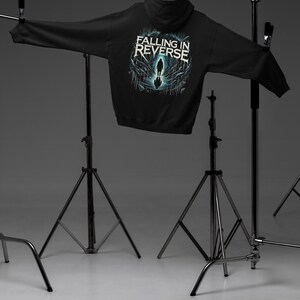 May include: Black hooded sweatshirt with a graphic print of a person walking on a cracked surface. The text "Falling in Reverse" is printed above the graphic.