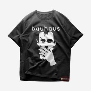 Puede incluir: Camiseta negra con un gráfico blanco de la cara de un hombre con la palabra "bauhaus" impresa encima.
