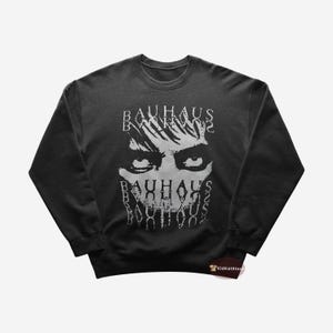 Puede incluir: Sudadera negra con un estampado gráfico blanco de una cara con la palabra "Bauhaus" repetida varias veces.