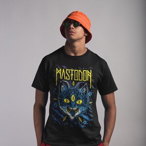May include: A black t-shirt featuring a blue and yellow illustration of a cat with three eyes and the word "MASTODON" in yellow lettering.