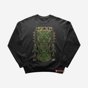 Puede incluir: Sudadera negra con un gráfico verde y dorado de una criatura con cuernos y una calavera. El texto "MASTODON" está por encima de la criatura.