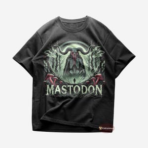 May include: Black t-shirt with a green and red illustration of a skeletal creature with horns and a full moon in the background. The text "MASTODON" is printed in white below the illustration.