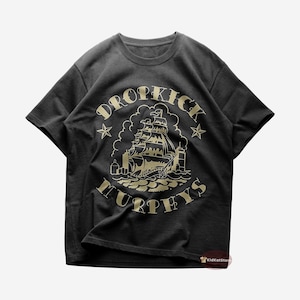 May include: Black t-shirt with a gold graphic featuring a sailing ship, waves, and the text "DROPKICK MURPHYS" in a circular design. Two gold stars flank the ship. The shirt is made of a soft material.