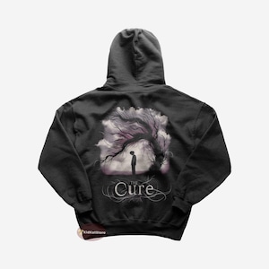 May include: A black hooded sweatshirt with a graphic print of a tree and a person standing in front of it. The text "The Cure" is printed below the image.