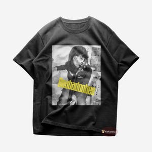 May include: Black t-shirt with a black and white image of a person holding a violin. The image has the text "abadootie" in yellow. This t-shirt is a casual wear item.