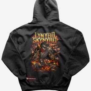 Puede incluir: Sudadera con capucha negra con un gráfico de los miembros de la banda Lynyrd Skynyrd como esqueletos en una escena de fuego. El nombre de la banda está en letras doradas. La sudadera tiene una capucha con cordón y un bolsillo tipo canguro.