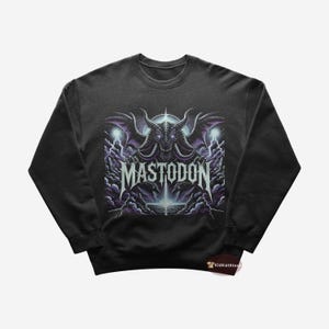 Puede incluir: Una sudadera negra con un estampado gráfico de un monstruo con alas y el texto "MASTODON" en blanco.
