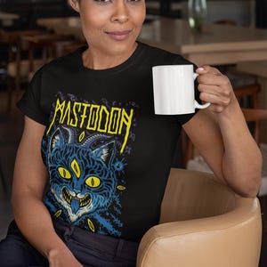 May include: A black t-shirt featuring a yellow and blue graphic of a three-eyed cat with horns and the text "Mastodon" above it.