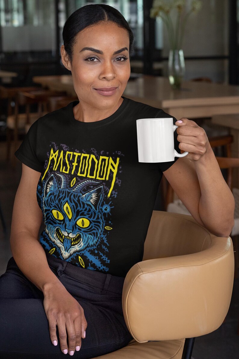 May include: A black t-shirt featuring a yellow and blue graphic of a three-eyed cat with horns and the text "Mastodon" above it.