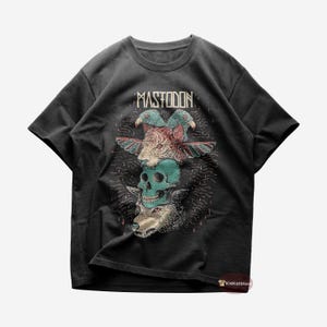 Puede incluir: Una camiseta negra con un estampado gráfico de una calavera, un lobo y pájaros. El texto "Mastodon" está impreso sobre el gráfico.