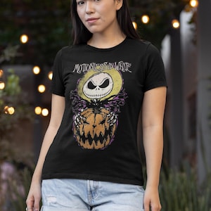 Może przedstawiać: Czarny T-shirt z grafiką Jacka Skellingtona z filmu Koszmar przed świętami trzymającego dynię. Tekst "Motionless in White" jest nadrukowany nad grafiką.