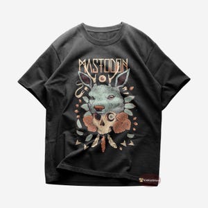 Puede incluir: Camiseta negra con un estampado gráfico de una calavera de ciervo con un ojo, rodeada de flores y plumas. El texto "Mastodon" está impreso sobre el gráfico.
