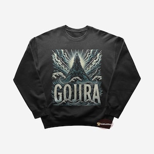 Op de afbeelding: Een donkergrijs sweatshirt met een grafische print van een bergtop die uit de oceaan golven oprijst. De tekst "GOJIRA" is in wit onder de berg gedrukt.