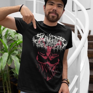 Könnte beinhalten: Ein schwarzes T-Shirt mit einem roten und weißen Grafikdruck eines Schädels mit dem Text "SLAUGHTER OF THE INNOCENT" darüber.
