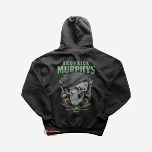 May include: A dark gray hooded sweatshirt with a graphic print of a skull wearing a green and black cap. The graphic includes the text "Dropkick Murphys" and "MCI.XVI. BOSTON, MA".