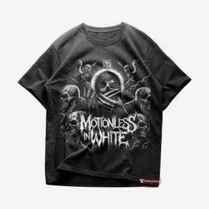 Może przedstawiać: Czarny T-shirt z białym nadrukiem zespołu "Motionless In White". Nadruk przedstawia czaszkę z ręką nad ustami i innymi czaszkami wokół niej.