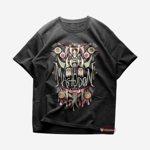 Puede incluir: Camiseta negra con un diseño gráfico detallado. El diseño incluye la palabra "MASTODON" en una fuente estilizada, junto con varias formas abstractas, círculos y líneas en tonos rojos, rosas y beige. Camiseta de manga corta.