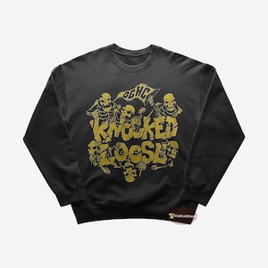 May include: Black sweatshirt with a gold graphic of skeletons holding a banner that says "OGHC Knocked Loose".