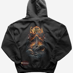 May include: Dark gray hoodie featuring a graphic design with the word "GOJIRA" in gold lettering above a detailed illustration of a skull, flames, and sea creatures. The design is centered on the back of the hoodie.