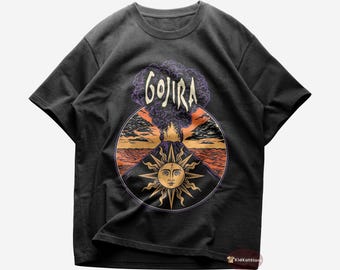 Può includere: T-shirt nero con una grafica di un vulcano in eruzione con un sole e la parola "GOJIRA" sopra.