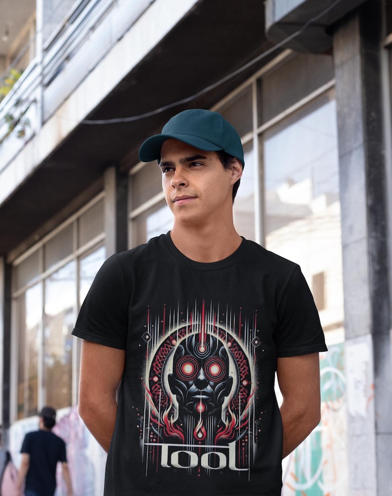 May include: A black t-shirt with a graphic of a stylized face with red eyes and the word "TOOL" printed below. The person wearing the shirt is wearing a dark blue baseball cap.