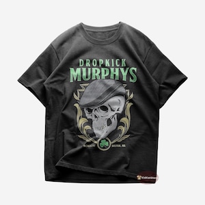 Peut inclure: T-shirt noir avec un graphique d'un crâne portant une casquette à motif vert et blanc. Le texte "Dropkick Murphys" est imprimé en vert et blanc au-dessus du crâne. Le texte "MCMLXXXVI BOSTON, MA" est imprimé sous le crâne.