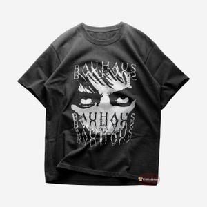 Puede incluir: Una camiseta negra con un gráfico blanco de la cara de una persona con la palabra "BAUHAUS" repetida en un patrón en capas.