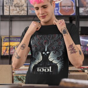 Puede incluir: Una camiseta negra con un estampado gr&aacute;fico de una figura oscura con l&iacute;neas en espiral y la palabra "TOOL" en letras blancas.