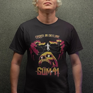 Op de afbeelding: Een zwart T-shirt met een grafische print van een schedel met een persoon die aan touwen boven hangt. De tekst "Order in Decline" en "Sum 41" staat op het shirt gedrukt.
