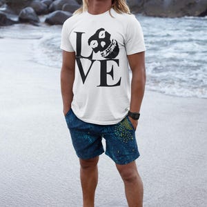 May include: A white t-shirt with a black graphic of a skull with the word "LOVE" printed on it. The person wearing the shirt is standing on a beach.