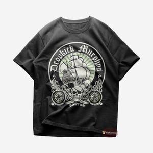 Könnte beinhalten: Schwarzes T-Shirt mit einem weißen Aufdruck eines Schiffes mit Totenkopf und Knochen. Der Aufdruck enthält den Text "Dropkick Murphys" und "Boston".