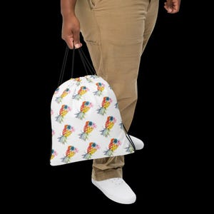 May include: White drawstring bag with a repeating pattern of colorful pineapples with flowers. The bag has black drawstrings.