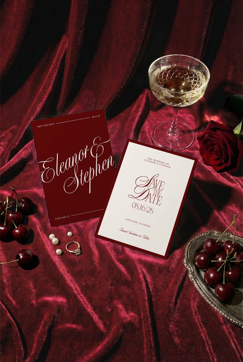 Op de afbeelding: Bordeaux trouwuitnodigingen met de namen "Eleanor & Stephen" en "Save the Date" op een rode fluwelen ondergrond. Een glas champagne, kersen, parels en een ring completeren de elegante sc&egrave;ne.