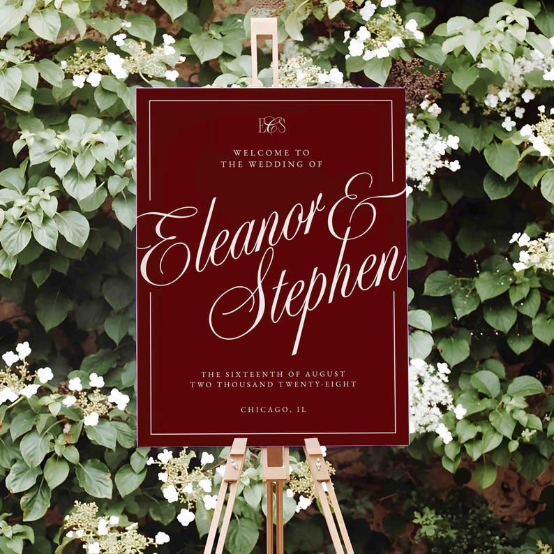 K&ouml;nnte beinhalten: Burgunderfarbenes Hochzeits-Willkommensschild auf einer Holzstaffelei. Das Schild zeigt eine elegante wei&szlig;e Schrift mit der Aufschrift &bdquo;Welcome to the Wedding of Eleanor & Stephen&ldquo;. Zus&auml;tzlicher Text enth&auml;lt Datum und Ort.