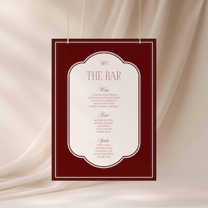 Puede incluir: Un letrero rectangular de men&uacute; de bar de color granate con un borde blanco y un interior blanco decorativo, suspendido por dos cuerdas finas. El letrero muestra "THE BAR" y enumera vinos, cervezas y licores.