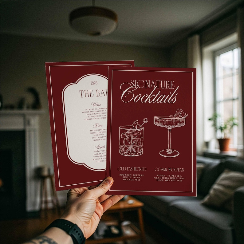 Puede incluir: Se sostienen dos men&uacute;s de c&oacute;cteles granates, que muestran las ofertas de un bar. El men&uacute; "Signature Cocktails" presenta ilustraciones de un Old Fashioned y un Cosmopolitan. El otro men&uacute; enumera vinos, cervezas y licores.