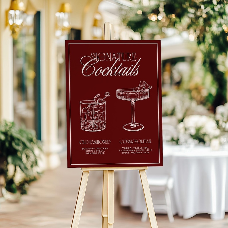 Puede incluir: Un letrero burdeos sobre un caballete de madera muestra "Signature Cocktails" en una elegante escritura. Debajo, ilustraciones representan un Old Fashioned y un Cosmopolitan, con sus ingredientes. El letrero est&aacute; al aire libre.