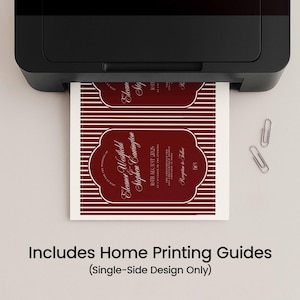 May include: A black printer printing a maroon and white invitation with the text "Eleanor Westfield Stephen Carrington" and "8th August 2025". The invitation has a decorative border and horizontal stripes. Two silver paper clips are on the surface.