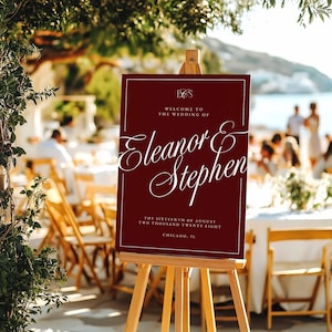 K&ouml;nnte beinhalten: Ein weinrotes Hochzeits-Willkommensschild auf einer Holzstaffelei. Das Schild zeigt eine elegante wei&szlig;e Schrift mit der Aufschrift "Eleanor & Stephen" sowie Details zu Datum und Ort der Hochzeit. Das Schild wird im Freien ausgestellt.