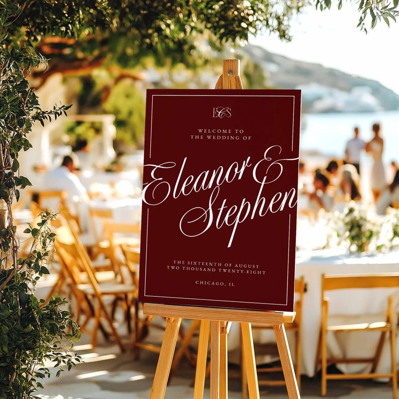 K&ouml;nnte beinhalten: Ein weinrotes Hochzeits-Willkommensschild auf einer Holzstaffelei. Das Schild zeigt eine elegante wei&szlig;e Schrift mit der Aufschrift "Eleanor & Stephen" sowie Details zu Datum und Ort der Hochzeit. Das Schild wird im Freien ausgestellt.