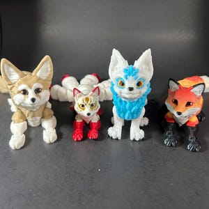 Puede incluir: Cuatro pequeñas figuritas de zorro, cada una con un esquema de color diferente. La primera es un zorro marrón con patas blancas, la segunda es un zorro blanco con patas rojas y una cara azul y blanca, la tercera es un zorro blanco con una cara azul y blanca, y la cuarta es un zorro rojo con patas negras.