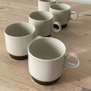 May include: Set of five white ceramic mugs with brown bands around the bottom. The mugs have a simple design and are perfect for everyday use.