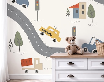 Puede incluir: Un mural de pared con una escena urbana de dibujos animados con carreteras grises, un coche azul, un taxi amarillo, un camión volquete rojo, semáforos, árboles y casas. Un oso de peluche marrón se sienta sobre una cómoda blanca de madera.