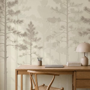 Op de afbeelding: Een houten bureau met een stoel, een lamp en boeken tegen een muur met behang in een lichtbeige en taupe bospatroon. Het behang toont silhouetten van dennenbomen in verschillende neutrale tinten, wat zorgt voor een gelaagd effect.