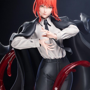 May include: A detailed figurine of a character with vibrant red hair, wearing a white shirt, black tie, and a black coat. The figure has a serious expression and is posed with hands outstretched. Red, flowing elements add a dynamic visual effect against a dark background.